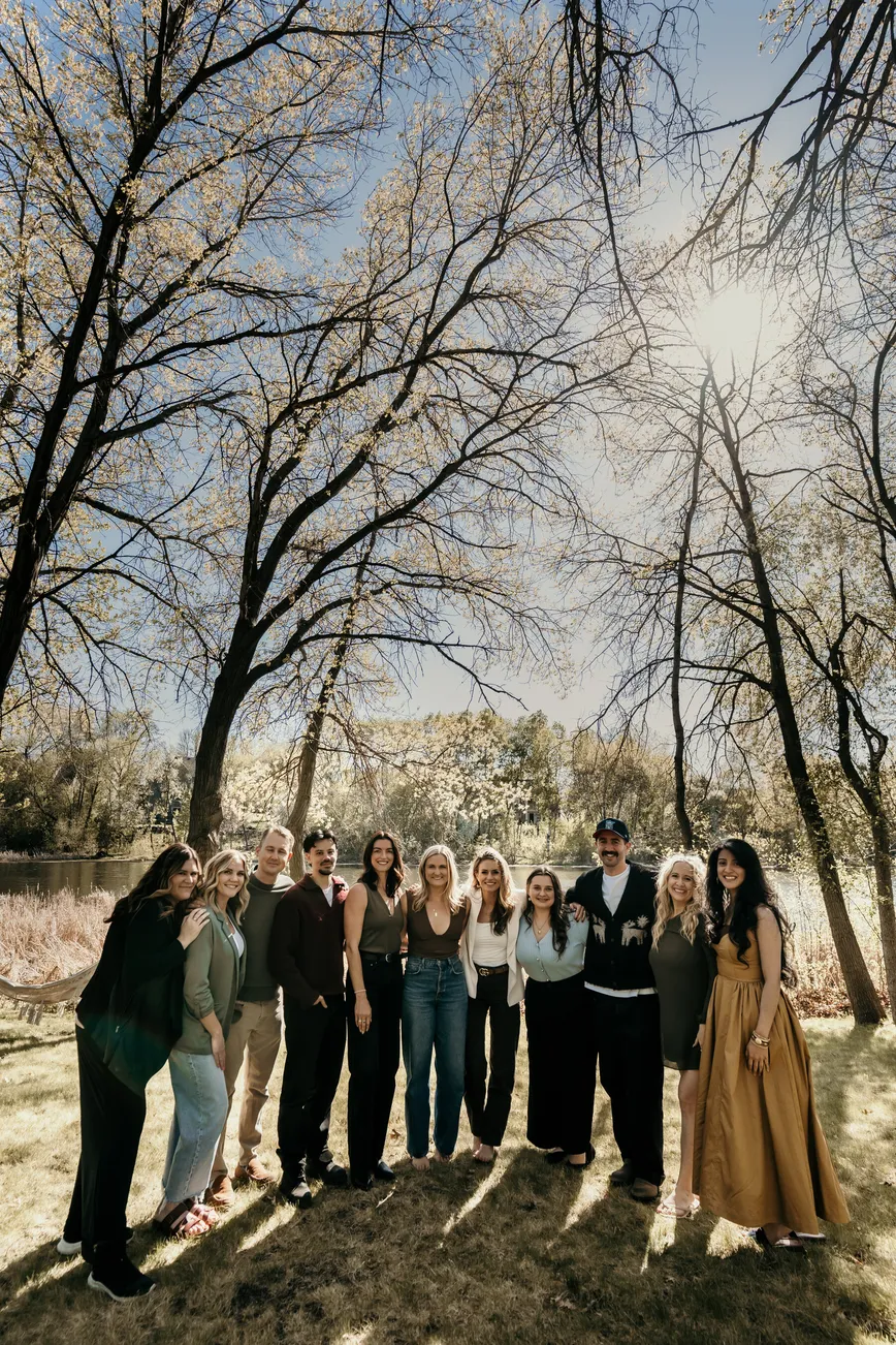 A group standing together outdoors beneath sunlit trees